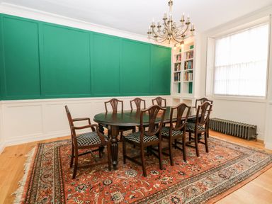A dining room with a dark wood table and eight chairs on an oriental rug next to a large window and built-in bookshelves at Enterprise House in Bury St Edmunds