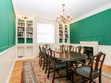 A dining room with a wooden table and chairs a chandelier bookshelves a fireplace and a carpet at Enterprise House in Bury St Edmunds