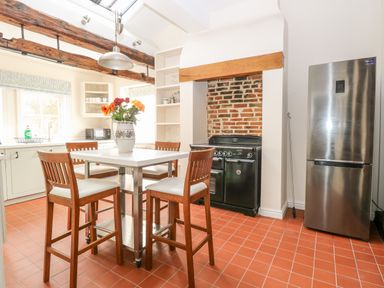 A kitchen with a high table and four chairs a stove in a brick alcove and a refrigerator at Enterprise House in Bury St Edmunds