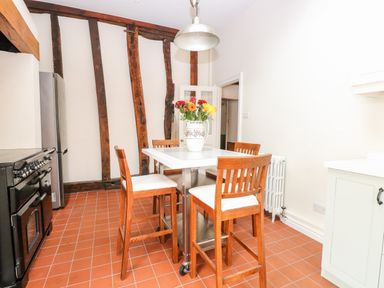 A kitchen with wooden beams on the wall wooden chairs around a white table and a vase with flowers at Enterprise House in Bury St Edmunds