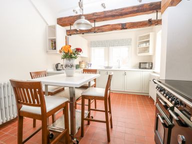 A kitchen with a white table and four wooden chairs a vase with flowers on the table wooden ceiling beams and a stainless steel stove at Enterprise House in Bury St Edmunds