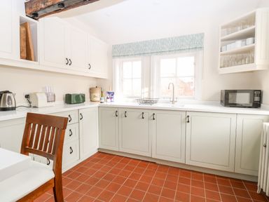 A kitchen with cabinets sink microwave window and a wooden chair at Enterprise House in Bury St Edmunds