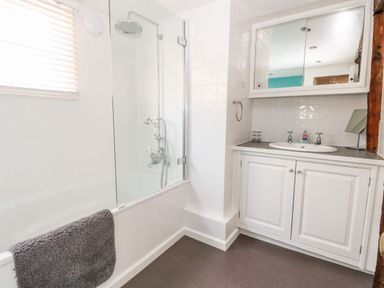 A bathroom with a bathtub shower combination and a sink with cabinet and mirror at Enterprise House in Bury St Edmunds