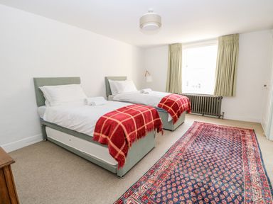 A bedroom with two single beds with red blankets and a patterned rug on the floor at Enterprise House in Bury St Edmunds