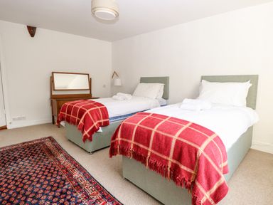 A bedroom with two single beds with red blankets a wooden dresser and a patterned rug at Enterprise House in Bury St Edmunds