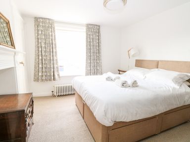A bedroom with a bed holding rolled towels a side table with a lamp and a chest of drawers at Enterprise House in Bury St Edmunds