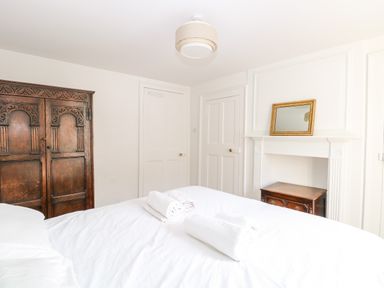 A bedroom with a bed with white linens and towels two white doors a wooden wardrobe and a mirror above a fireplace at Enterprise House in Bury St Edmunds