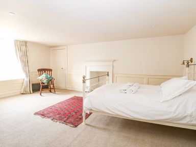 A bedroom with a single bed white bedding a wooden chair with a cushion a red rug and curtains at Enterprise House in Bury St Edmunds