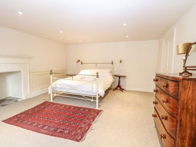 A bedroom with a white metal bed, red rug, wooden dresser, and two bedside tables at Enterprise House in Bury St Edmunds