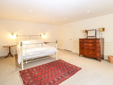 A bedroom with a white metal bed frame a red rug a wooden dresser with a mirror and lamps and a small round wooden table at Enterprise House in Bury St Edmunds