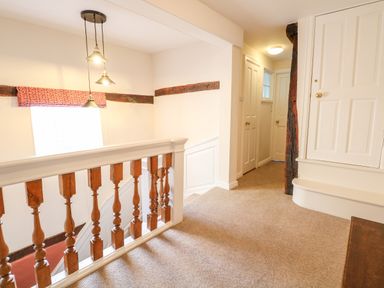 A hallway with stairs railing wooden beams multiple white doors and carpeted floor at Enterprise House in Bury St Edmunds
