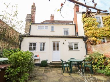A paved backyard with a green plastic table and chairs in front of a white two-story house at Enterprise House in Bury St Edmunds