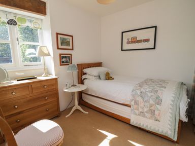 A bedroom with a single bed wooden dresser small round table and framed pictures at Crosscombe Barn in Loddiswell