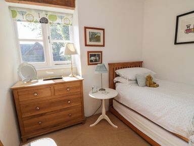 A bedroom with a wooden bed, side table with a lamp, wooden chest of drawers with a lamp, and window at Crosscombe Barn in Loddiswell
