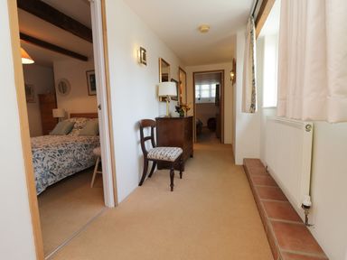 A hallway with a chair a chest of drawers and lamp with bedrooms visible at Crosscombe Barn Loddiswell