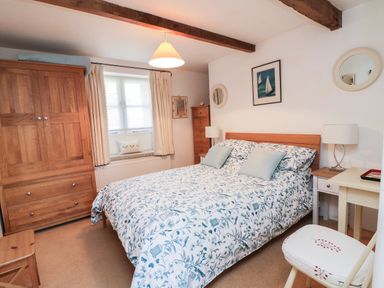 A bedroom with a bed with floral bedding a wooden wardrobe bedside tables and a window at Crosscombe Barn in Loddiswell