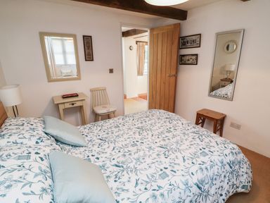 A bedroom with a double bed pillows small table chair mirror and wooden door at Crosscombe Barn in Loddiswell