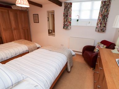 A bedroom with two single beds a wooden wardrobe a red armchair and a wooden dresser at Crosscombe Barn in Loddiswell