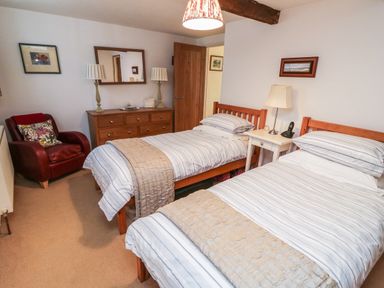 A bedroom with two single beds a wooden dresser a red armchair a bedside table with a lamp and telephone at Crosscombe Barn in Loddiswell