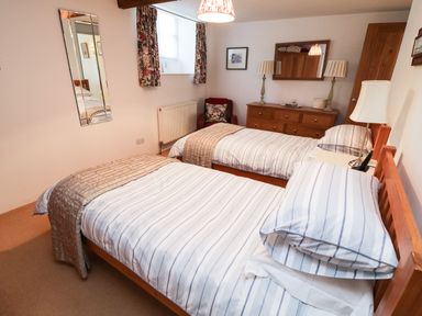 A bedroom with two single beds a wooden dresser and a window with curtains at Crosscombe Barn in Loddiswell