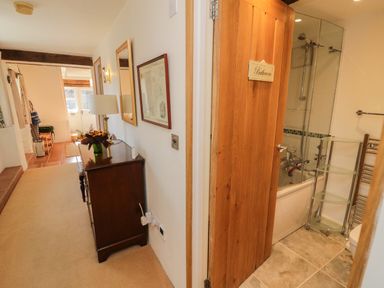 A hallway with a wooden dresser and a lamp next to a bathroom with a wooden door and a shower at Crosscombe Barn in Loddiswell