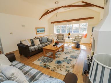 A living room with sofas, armchairs, a wooden coffee table, floral rug, and large windows at Crosscombe Barn in Loddiswell