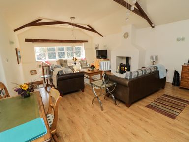A living room with sofas, armchairs, a coffee table, a fireplace, a television, and a dining table with chairs at Crosscombe Barn in Loddiswell