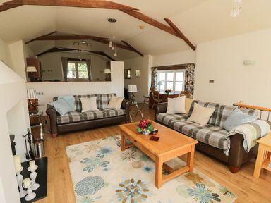 A living room with two plaid sofas a wooden coffee table and a dining table near a window at Crosscombe Barn in Loddiswell
