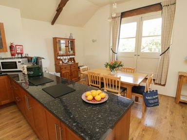 A kitchen with a black countertop island and wooden dining table by glass doors at Crosscombe Barn in Loddiswell