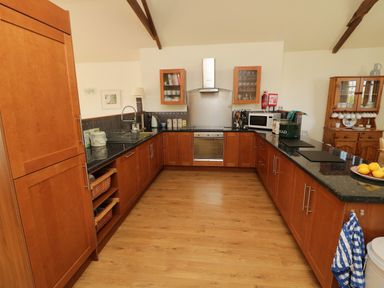 A kitchen with wooden cabinets black countertops a stove a microwave and a wooden cabinet in Crosscombe Barn in Loddiswell