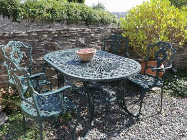 An outdoor patio with a metal table and four matching chairs and a potted plant on the table at Crosscombe Barn in Loddiswell