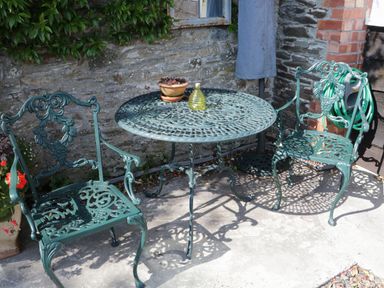 An outdoor patio with two green metal chairs and a matching round table with a small plant and bottle at Crosscombe Barn in Loddiswell