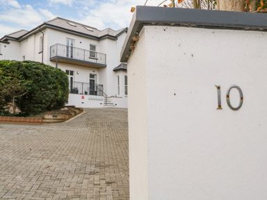 The exterior of a white house with balconies and a driveway with a white wall showing the number 10 Riviera Heights Paignton