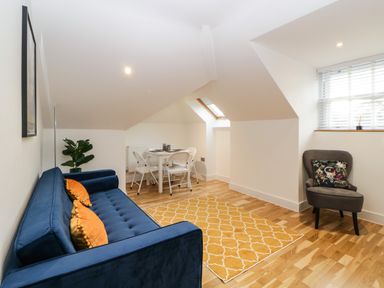 A room with a blue sofa with orange cushions a yellow rug a dining table with white chairs a grey armchair and a window with blinds at Riviera Heights in Paignton