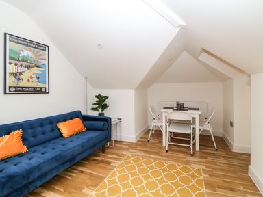 A living room with a blue sofa orange pillows a small dining table with white chairs and a yellow rug at Riviera Heights in Paignton