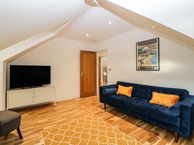 A room with a blue sofa with orange pillows a patterned yellow rug a wooden floor a TV on a white stand and a wooden door at Riviera Heights in Paignton