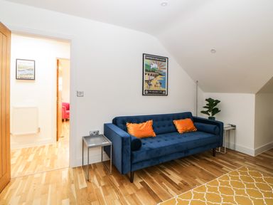 A room with a blue sofa with orange cushions a small table a plant and a framed poster on the wall at Riviera Heights in Paignton