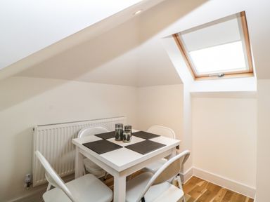 A dining area with a white table four white chairs placemats and a window at Riviera Heights in Paignton