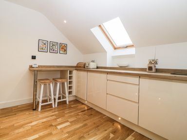 A kitchen with two stools under a wooden countertop and three framed fruit prints on the wall at Riviera Heights in Paignton