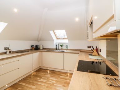 A kitchen with wooden countertops white cabinets a stovetop a sink under a skylight window and kitchen appliances at Riviera Heights in Paignton
