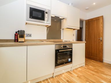A kitchen with white cabinets a microwave oven knives on a wooden block and a wooden door at Riviera Heights in Paignton