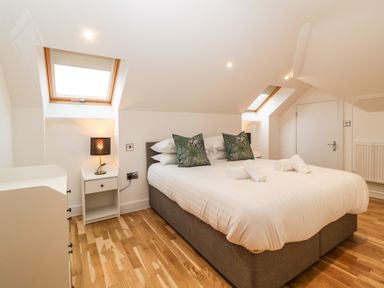 A bedroom with a double bed white bedding wooden floor bedside tables lamps and skylight windows at Riviera Heights in Paignton