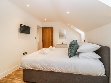 A bedroom with a bed pillows and rolled towels a TV mounted on the wall a dresser with a mirror and a wooden door at Riviera Heights in Paignton