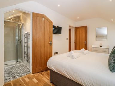 A bedroom with a bed towels on it a wooden door leading to a bathroom with a shower and a TV on the wall at Riviera Heights in Paignton