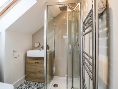 A bathroom with a glass shower enclosure a wooden cabinet with a sink a small round mirror a towel rail and patterned floor tiles at Riviera Heights in Paignton