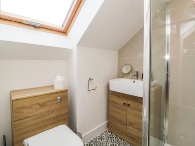 A small bathroom with a toilet a wooden cabinet a sink with cabinet a round mirror and a glass shower at Riviera Heights in Paignton