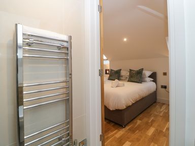 View from a bathroom with a towel radiator into a bedroom with a double bed pillows and wooden floor at Riviera Heights Paignton
