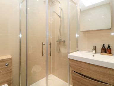 A bathroom with a glass shower enclosure a wooden sink cabinet and a wall cabinet at Riviera Heights in Paignton