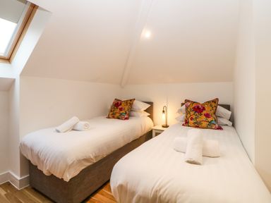 A bedroom with two single beds white linens floral pillows rolled towels and a lamp on a nightstand at Riviera Heights in Paignton