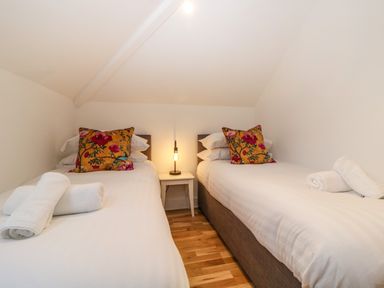 A small bedroom with two single beds with white linens and floral pillows with a small bedside table and lamp in between at Riviera Heights in Paignton